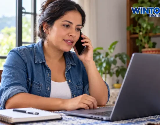 Mujer hablando por teléfono frente a un computador portátil en su hogar.