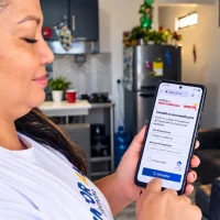 Madre colombiana consulta desde su celular información sobre beneficiarios de Ingreso Mínimo Garantizado en Bogotá.